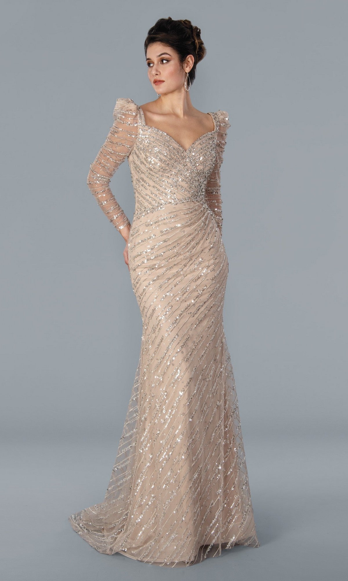 A woman poses against a plain gray background wearing the Stella Couture 22365—a champagne long formal dress featuring silver sequin stripes, sheer long sleeves, and a sweetheart neckline.